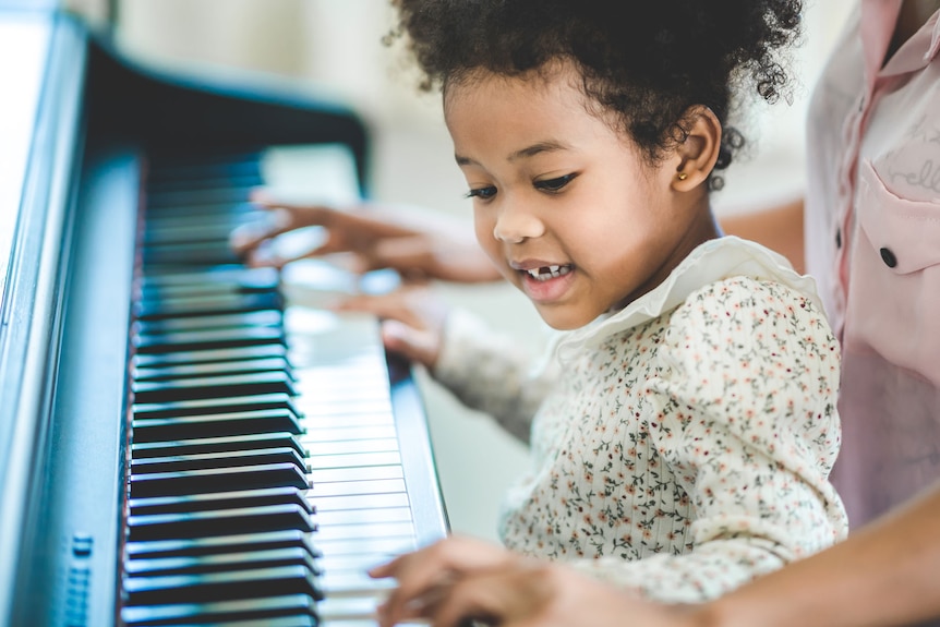 A young girl sits in her mother's lap as she practises piano.