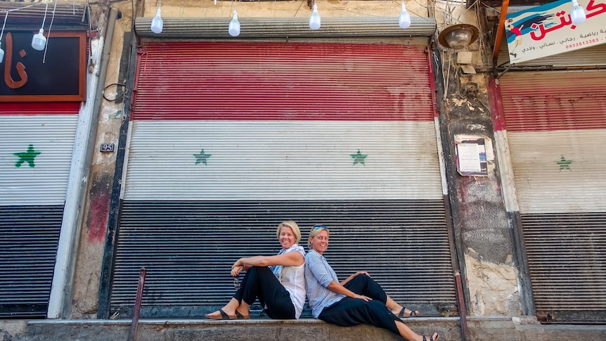 Two travellers sitting infront of the Syria flag mural 