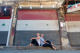 Two travellers sitting infront of the Syria flag mural 