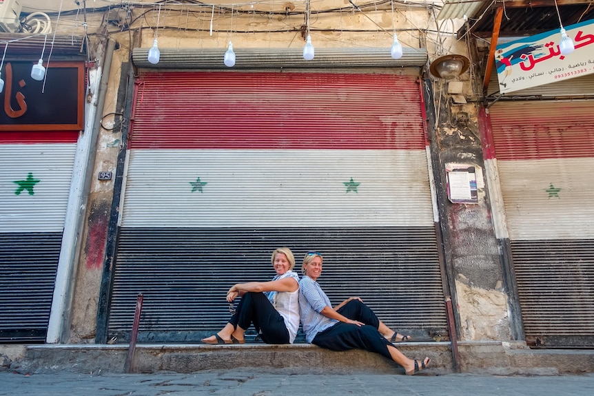 Two travellers sitting infront of the Syria flag mural 