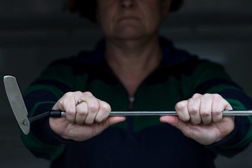 The partly obscured face of homeless woman 'Stephanie' grasping a golf club she keeps on hand for self defence.