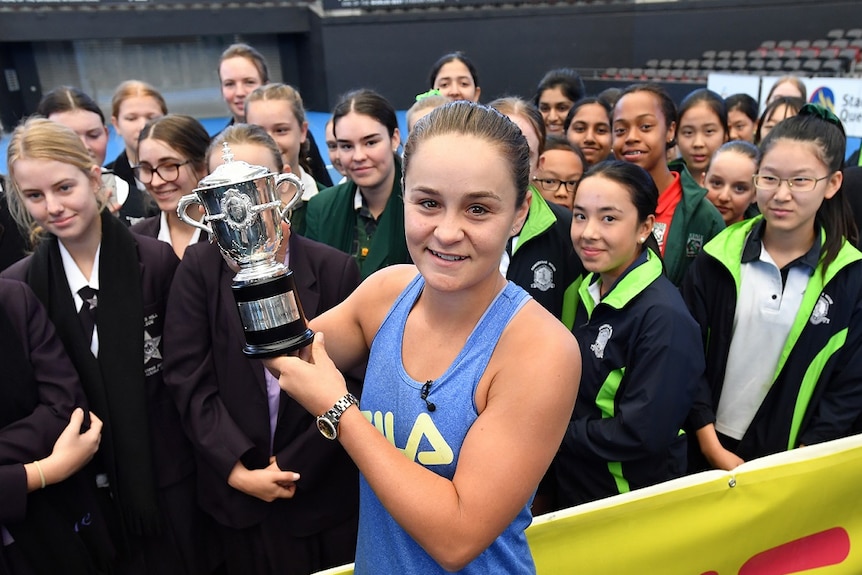 Barty holds the French Open trophy while surrounded by junior players at the Pat Rafter Arena in Brisbane.