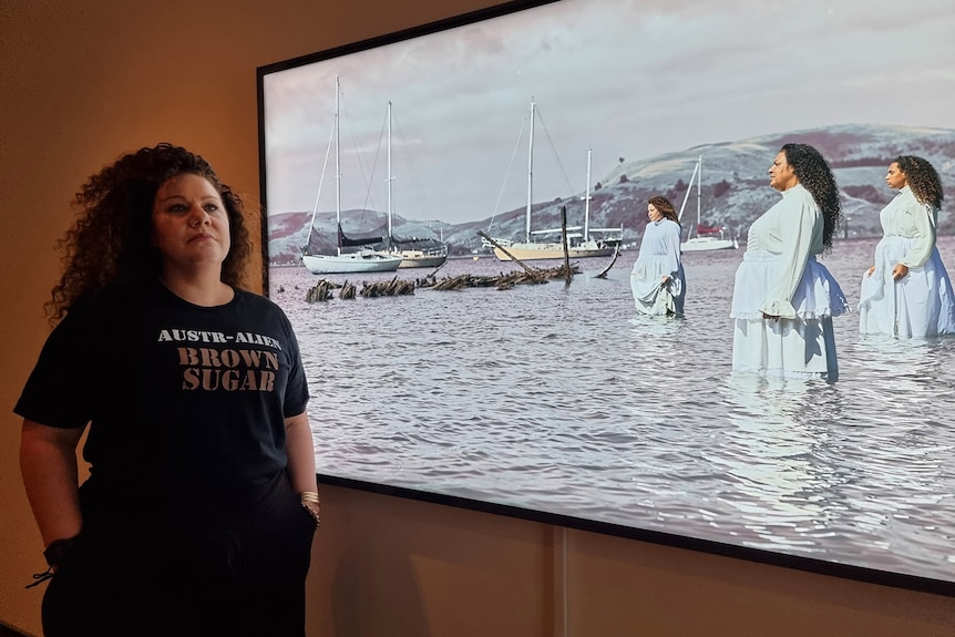 A woman stands in front of a light-box photo in an art gallery