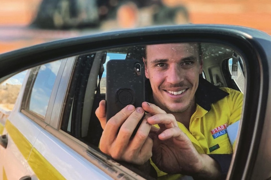 A man taking a photo of himself through the reflection of a car side mirror