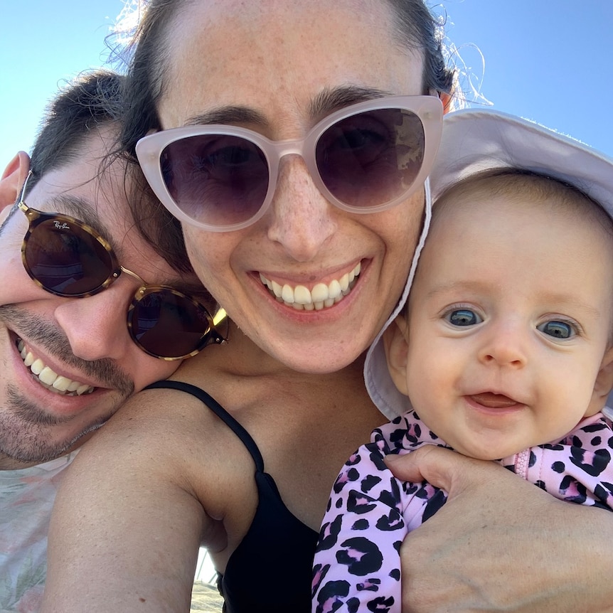 A woman and a man cuddle their baby at a beach.