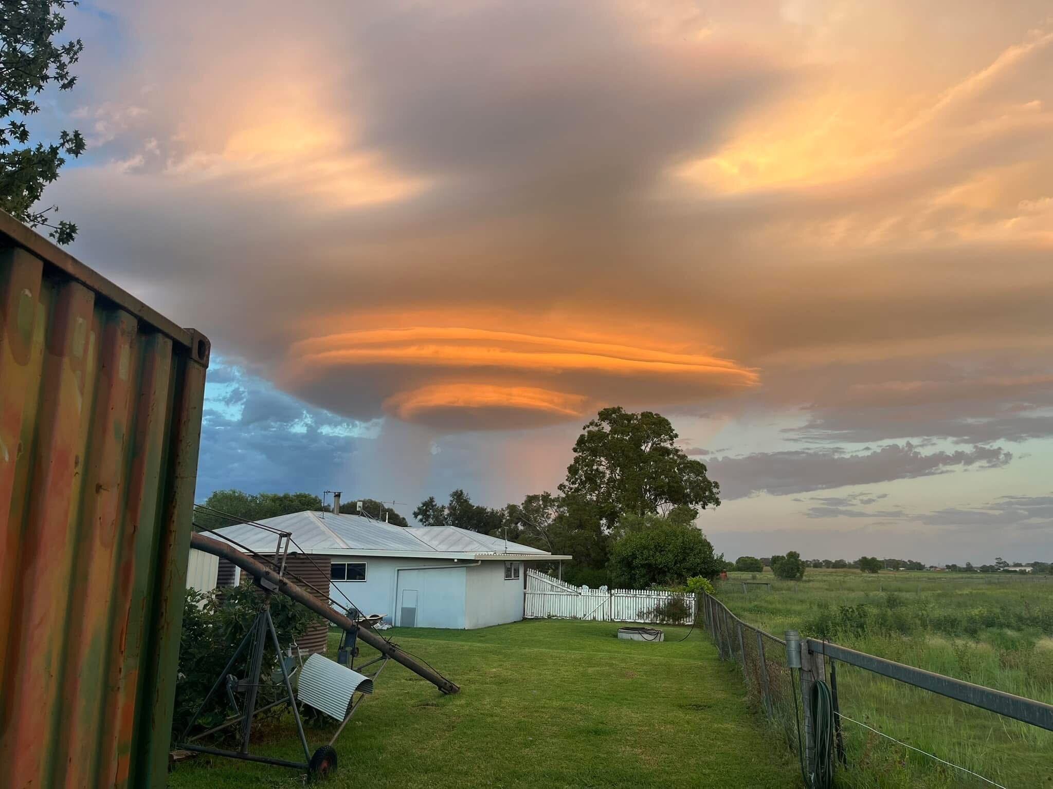 Orangey clouds in the shape of a shelf sitting in the sky above a rural property.