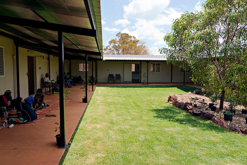 The courtyard of a shared accommodation building, featuring green grass, some rocks and trees surrounded by a verandah.