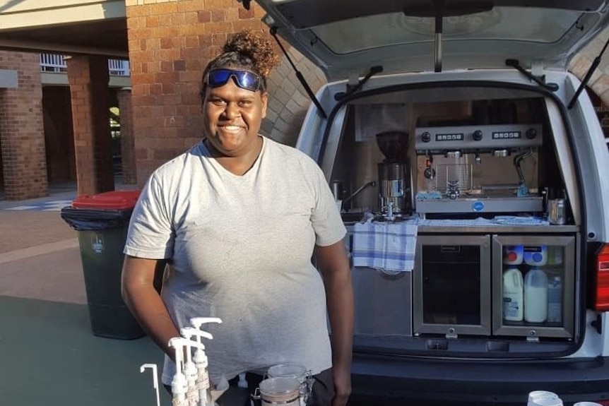 Naz Wapau stands in front of a table with the open coffee van behind her.