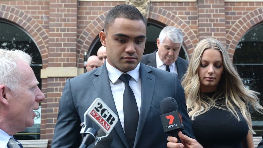 An NRL player and his fiancee are surrounded by microphones as they leave a court.