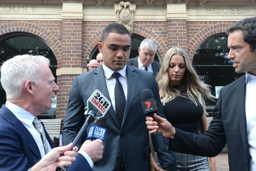 An NRL player and his fiancee are surrounded by microphones as they leave a court.