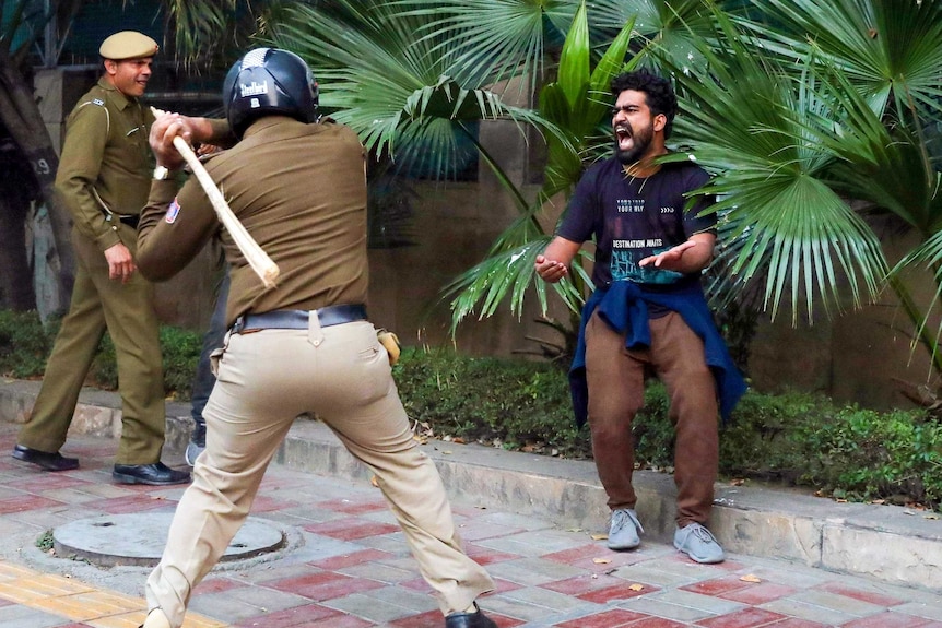 A man shouts and gestures in front of a policeman about to swing a bamboo cane