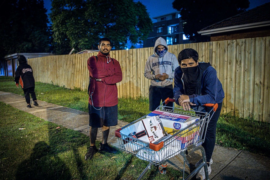 Three men, two with facemasks, and a trolley full of alcohol.