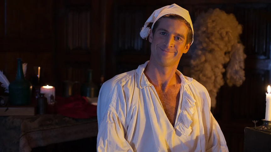 A man wearing a historic nightgown and hat smiling