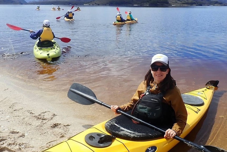 A woman sits in a yellow kayak and holds a paddle