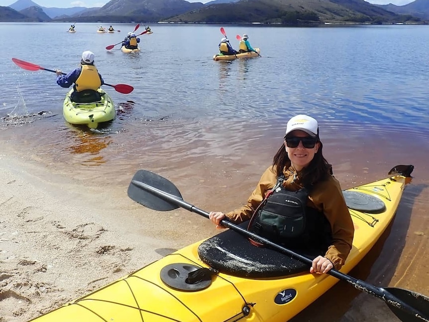 A woman sits in a yellow kayak and holds a paddle