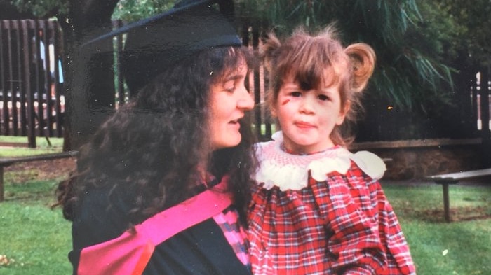 Jessica Amelia as a child is held by her mother, who is wearing a black graduation gown and cap.