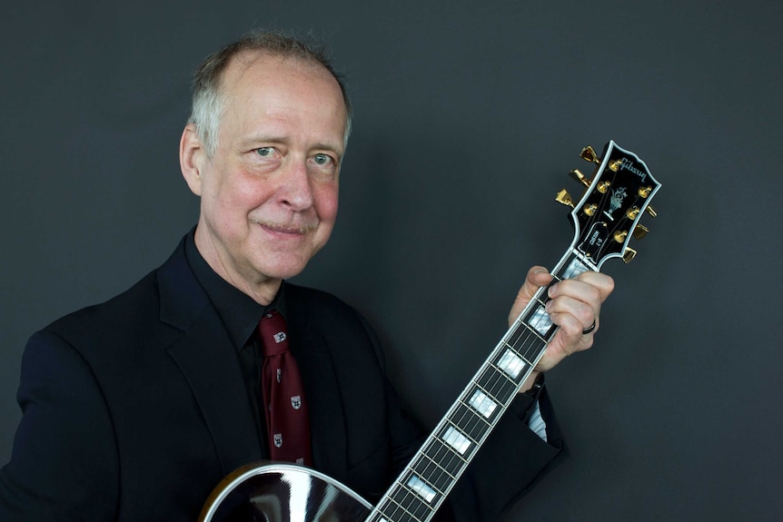 Henry Juszkiewicz smiles at the camera while holding a Gibson guitar