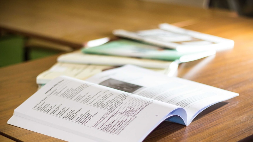 An open book sits on a table with other books lying next to it.