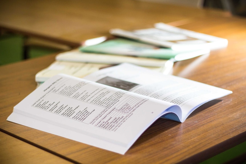 An open book sits on a table with other books lying next to it.