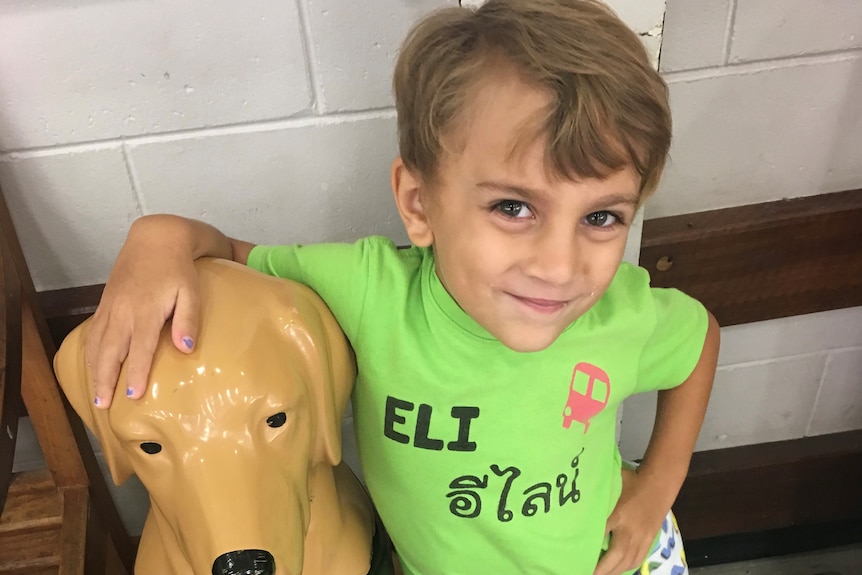 a child smiles at the camera while wearing a green shirt that says 'Eli'