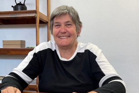 Tracy Norman pictured in doors smiling with her arms resting on a table.