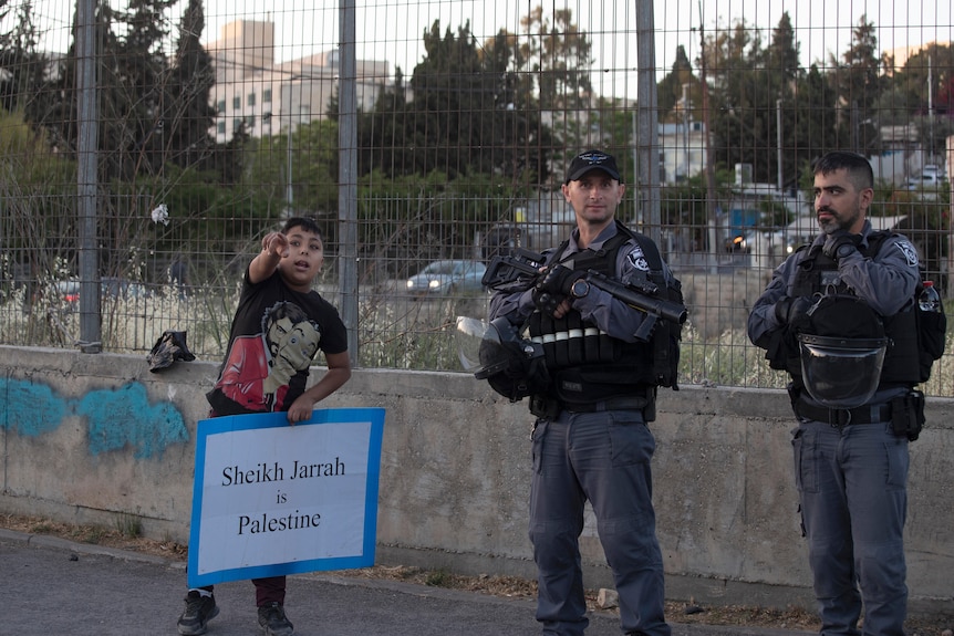A Palestinian boy speaks to police while holding a placard reading 'Shiekh Jarrah is Palestine'