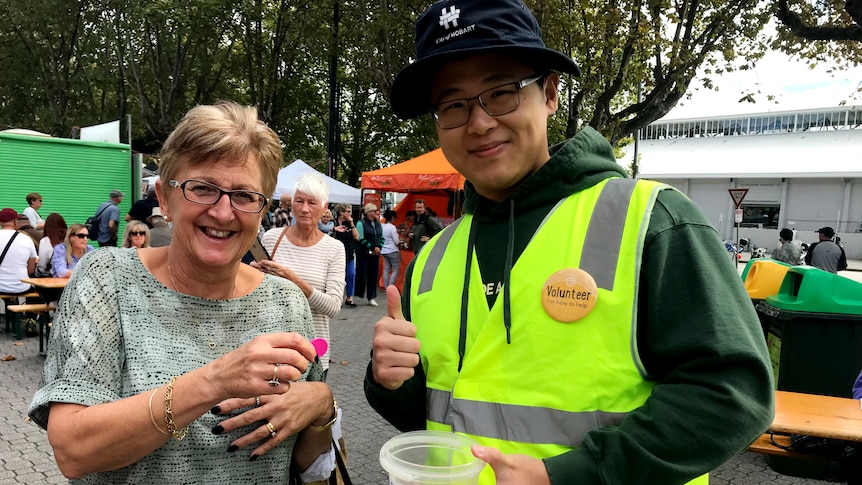A white woman and a Chinese man smiling at the camera. He wears a badge saying volunteer.
