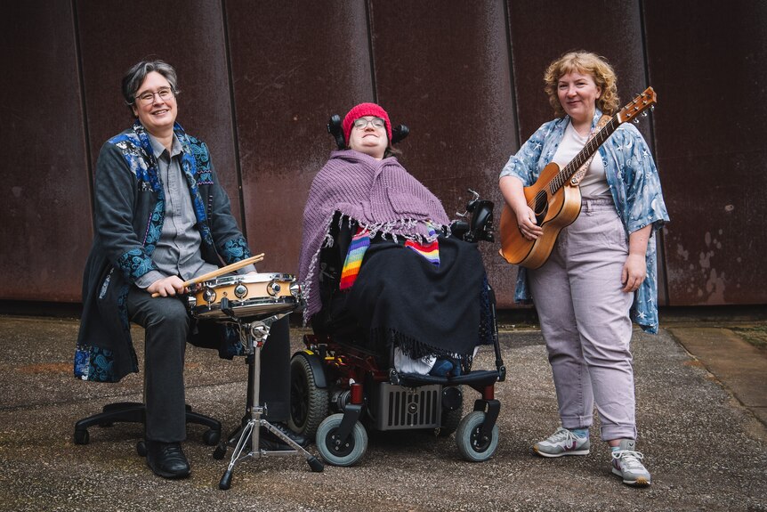 Three women holding instruments, the one is the middle sits in a wheelchair 