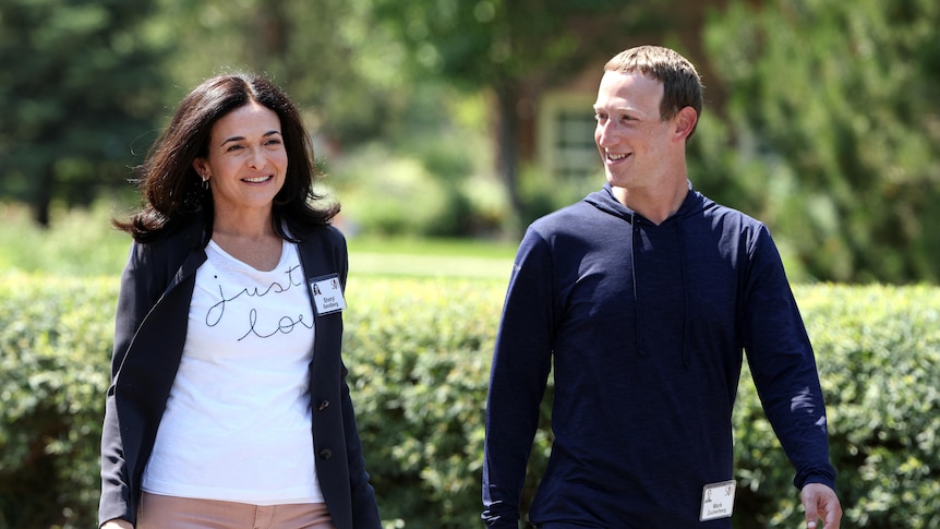 A white woman (Sheryl Sandberg) with long dark hair walks next to a white man with short hair (Mark Zuckerberg), casual clothing