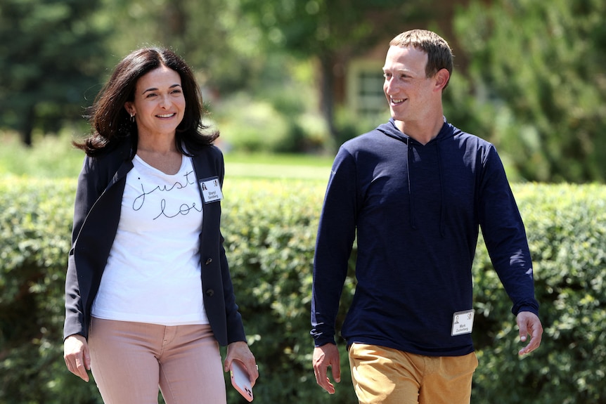 A white woman (Sheryl Sandberg) with long dark hair walks next to a white man with short hair (Mark Zuckerberg), casual clothing