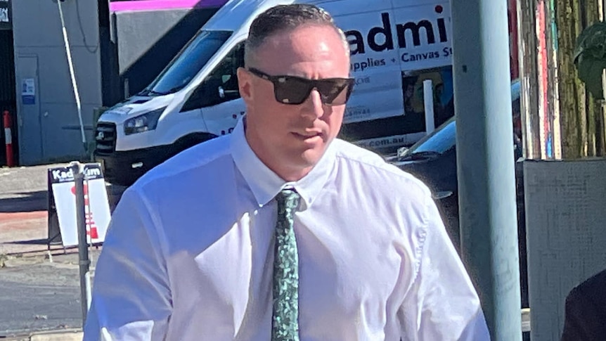 travis paul pocock wearing a white shirt and approaching a court house 