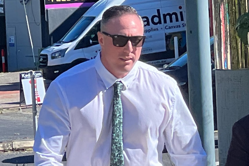 travis paul pocock wearing a white shirt and approaching a court house 