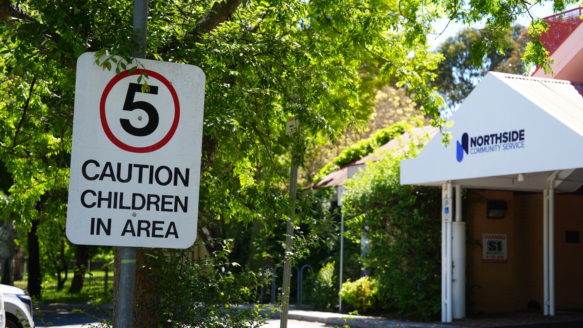 Daycare building with surrounding trees and a traffic sign that says '5 Caution Children in Area'