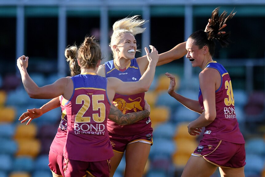 Four Brisbane Lions AFLW players embrace as they celebrate a goal against Collingwood.