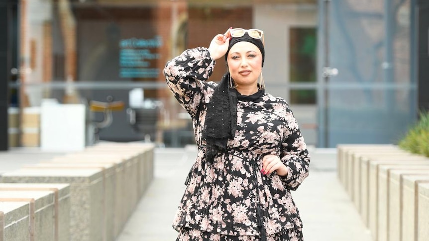 A photo of AIsha wearing hijab, in a floral dress, and wearing sunglasses over her scarf.