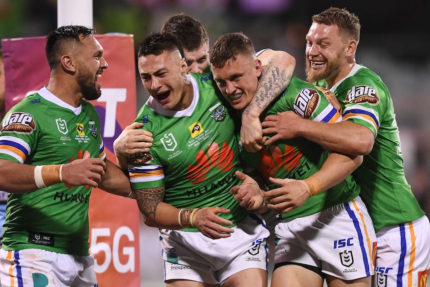 Five Canberra Raiders NRL players embrace as they celebrate a try against the Sharks.