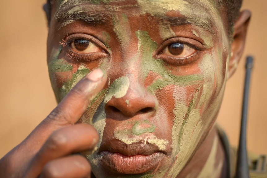 Closeup of Akashinga ranger, putting green facepaint on one cheek.