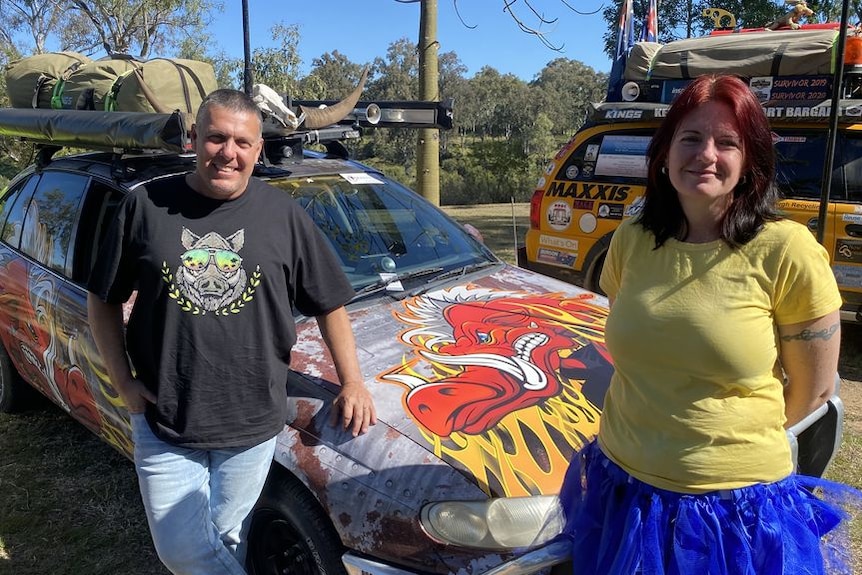 A man and a woman in colourful clothes stand either side of a decorated car
