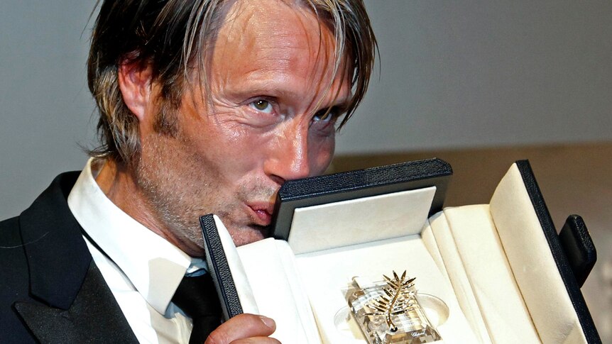 Mads Mikkelsen kisses his Best Actor award at Cannes.