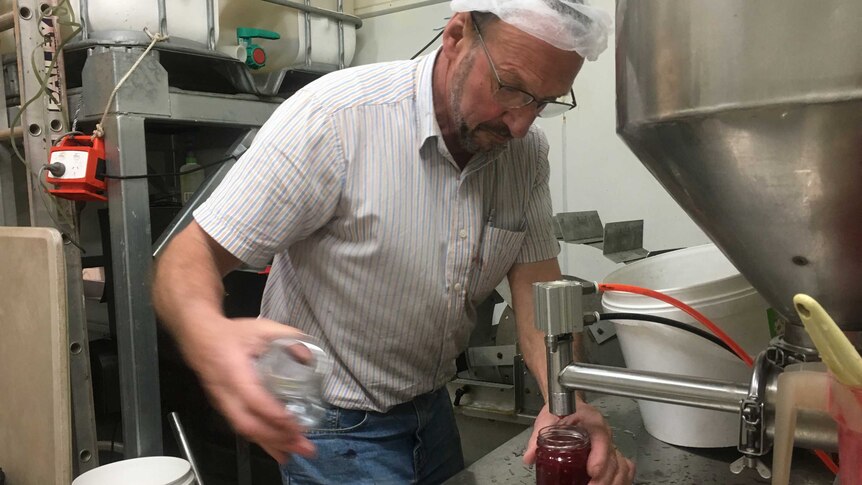 a large stainless steel machine fills jam jars.