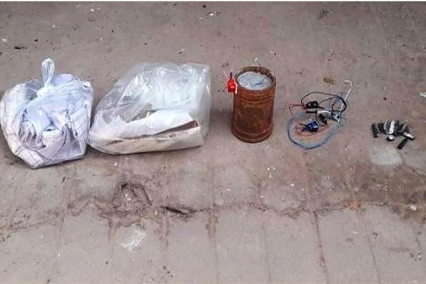 Plastic bags filled with items sent to prisones sit next to a bomb made out of a rusty can.