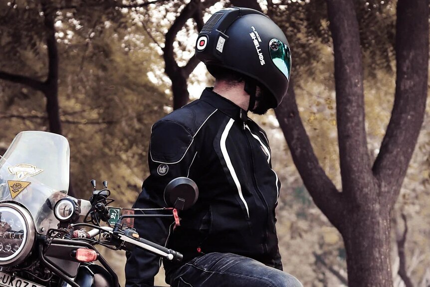 Un homme se tient à côté d'une moto tout en portant un casque de moto noir futuriste.