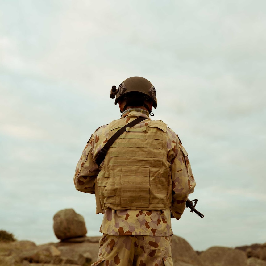 A special forces soldier holding a weapon looks out over rocks