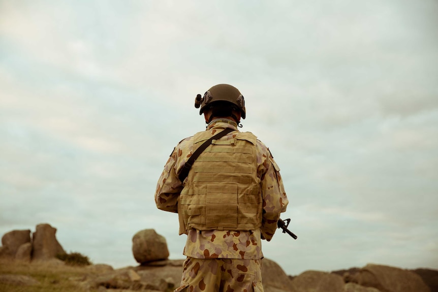 A special forces soldier holding a weapon looks out over rocks