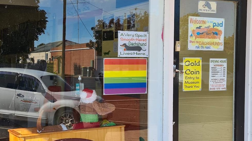A glass window with various signs including a pride flag. 