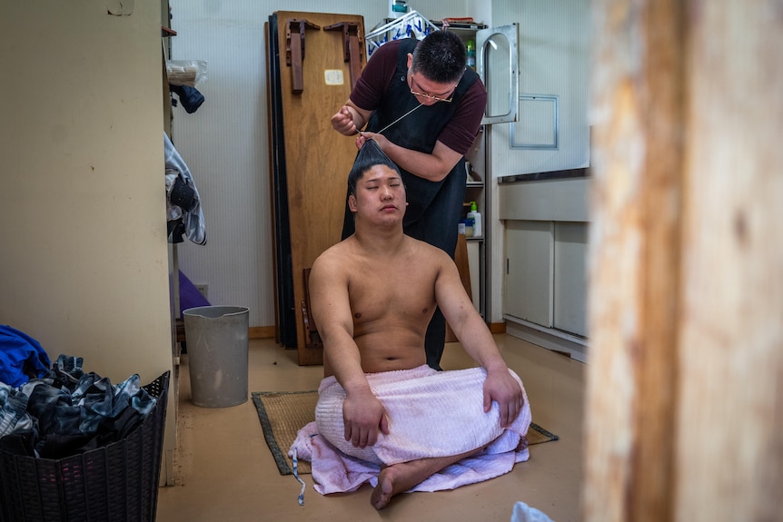 A Japanese man gets his hair done by another man