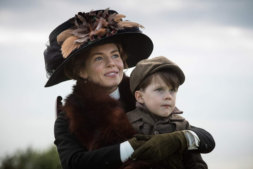 Still image of Sienna Miller with child actor Tom Mulheron seated on her lap, from the film The Lost City of Z.