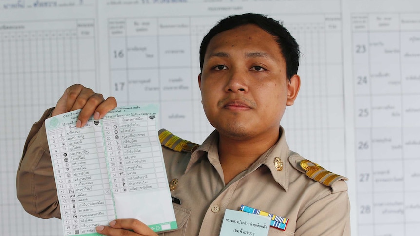 A Thai official wearing a karki uniform holds up a ballot sheet