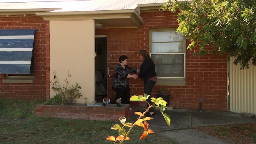 Two women stand outside a red brick house