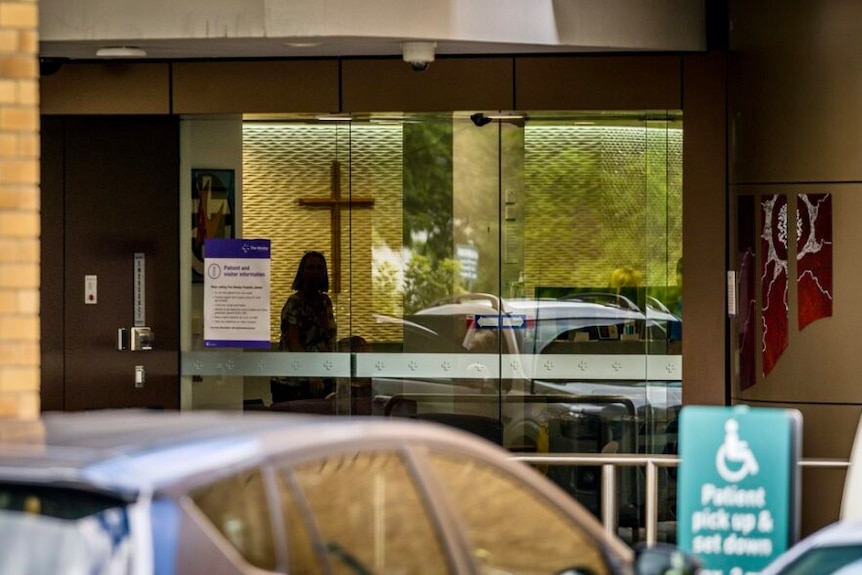 Glass entrance doors show a cross on the wall inside The Wesley Hospital.